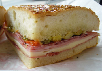 Muffaletta cross-section shows thick, chewy bread holding cheese, cold cuts, and oily olive salad