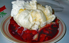 A giant slice of cherry pie occupies a full plate and is topped with a half-pint of vanilla ice cream.