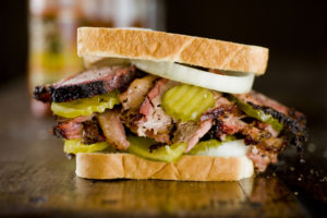 BBQ brisket is sandwiched with pickles and onions.