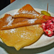3 folded-over, paper-thin pancakes accompanied by a globe of pink lingonberry butter