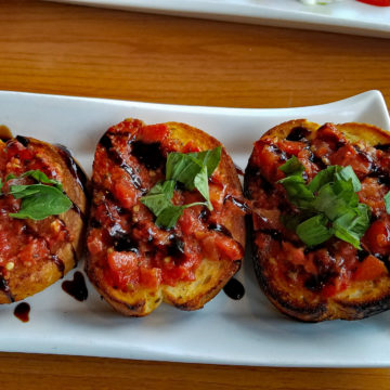 Three tiles of grilled toast topped with fruity tomatoes, basil, and a balsamic glaze