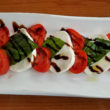 A row of tomato slices, mozzarella cheese, and basil drizzled with balsamic vinegar