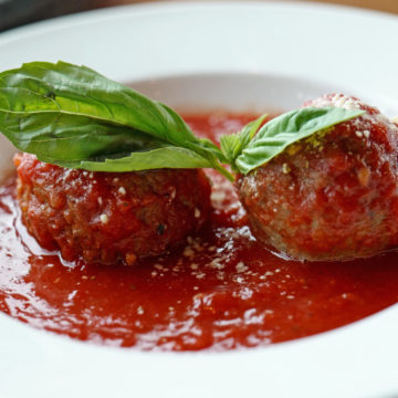 Pair of meatballs in tomato sauce, topped with fresh basil
