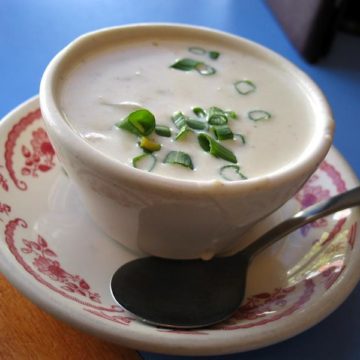 A bowl of thick, creamy chowder, loaded with clams and sprinkled with green onion