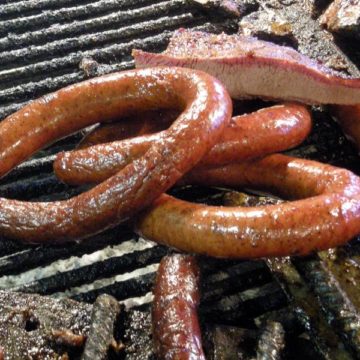 Long curls of sausage bask in smoke atop a wood grill