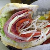 Cross section of a hoagie with salami, ham & provolone, garnished with lettuce, tomato, and onion, sprinkled with oil and spice