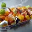 Plastic tray holds a variety of fruits sprinkled with pepper.