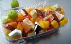 Plastic tray holds a variety of fruits sprinkled with pepper.