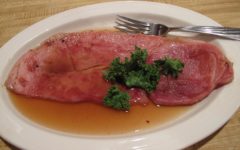 A plate-size slice of country ham is bathed in caramel-colored red-eye gravy