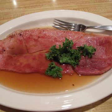 A plate-size slice of country ham is bathed in caramel-colored red-eye gravy