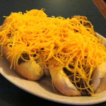Two bunned hot dogs covered with chili and shredded cheddar cheese