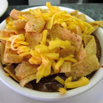 Bowl of chili is topped with Fritos and shredded cheese