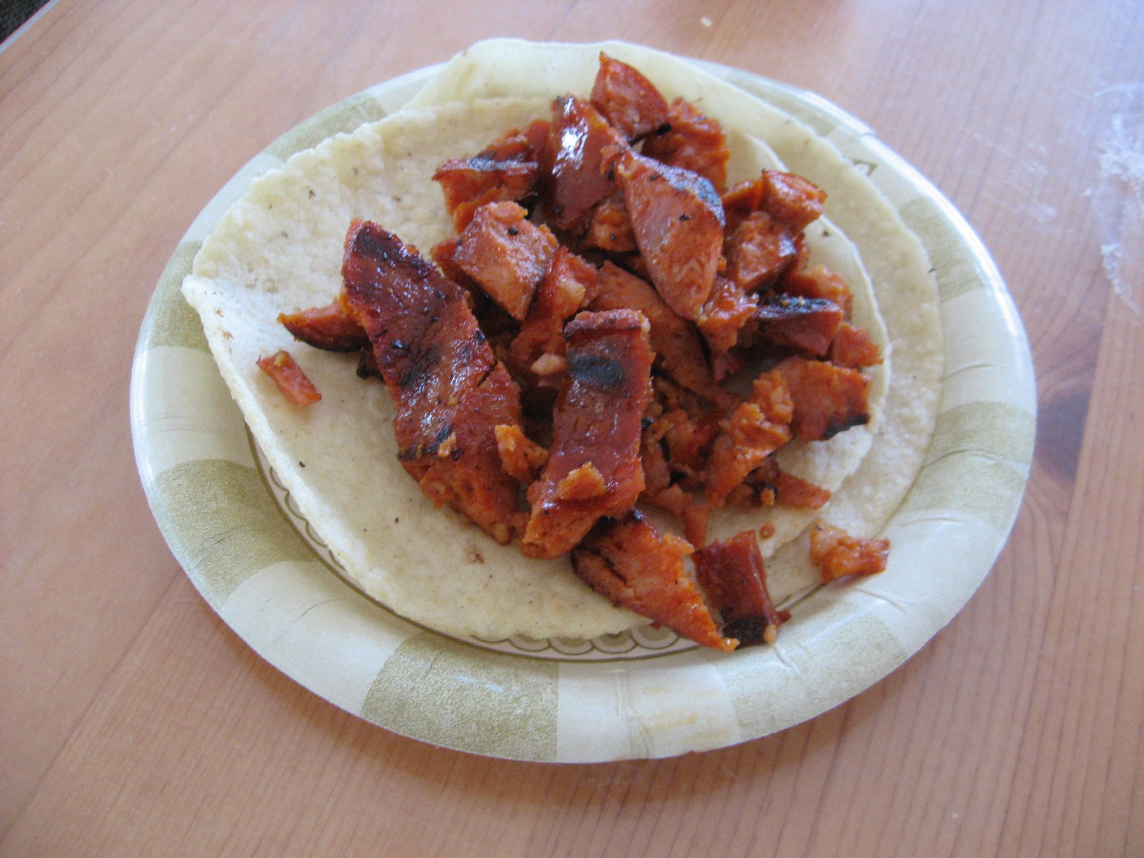 Spice-red chorizo sausage spread out on tortillas on a paper plate