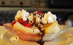 Glass soda fountain boat holds scoops strawberry, chocolate, and vanilla ice cream topped with sauce, nuts, and whipped cream, shored in by bananas sliced lengthwise