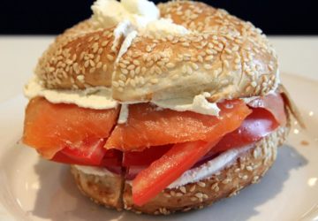 Sesame bagel is stuffed with lox, tomato slices, and cream cheese.