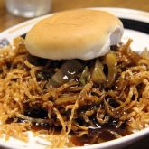 Sandwich of chow mein with crisp noodles spills out of its bun.