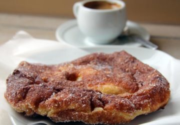 Flat, sugar-dusted disk of quick-fried pastry with a cup of espresso