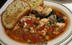 Bowl full of seafood in herbed tomato sauce, accompanied by toasted sourdough bread