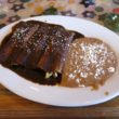 A trio of rolled enchiladas is covered with dark, rich mole sauce and accompanied on the plate by refried beans.