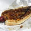 A big Polish sausage, smothered with fried onions, extends beyond the length of its bun.
