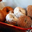 A basket of six hot donuts: plain, powdered sugar, cinnamon