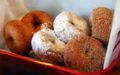 A basket of six hot donuts: plain, powdered sugar, cinnamon