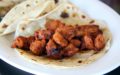 Chile-red chunks of marinated pork spill out of a folded-over tortilla