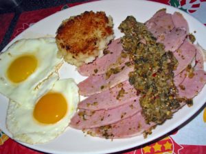 Breakfast plate features eggs, a mashed potato cake, and greens-topped ham.
