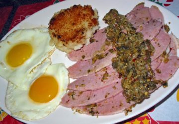 Breakfast plate features eggs, a mashed potato cake, and greens-topped ham.