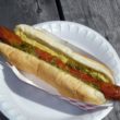Well-dressed foot-long hot dog extends beyond its bun.