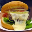 Molten cheese oozes off a tender burger in a bun with lettuce, tomato, and sliced onion at Ted's in Meridian, CT
