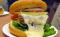 Molten cheese oozes off a tender burger in a bun with lettuce, tomato, and sliced onion