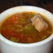 Cup is filled with green chilies, tomatoes, and chunks of pork in spicy broth