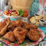 Large platter of fried chicken is backed by biscuits and fruit salad