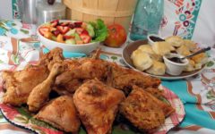 Large platter of fried chicken is backed by biscuits and fruit salad