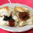Two hot biscuits on a plate, opened up and dolloped with blackberry preserves and peach preserves