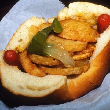 Capacious bun holds two hot dogs, potatoes, peppers, and onions.