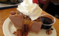 A wedge of icebox pie composed of ice cream, caramel, and nuts, topped with whipped cream, and with chocolate sauce on the side