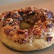Donut is plastered with maple frosting and covered with countless pieces of bacon