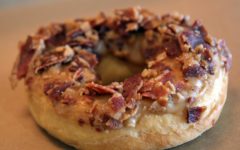 Donut is plastered with maple frosting and covered with countless pieces of bacon
