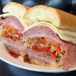Cold cuts, cheeses, and vegetables are piled high inside a long tube of Italian bread.