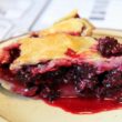 Wine red blackberries spill from a wedge of pie