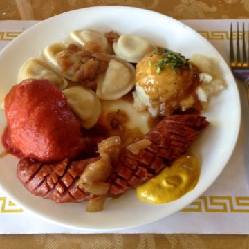 Bountiful Polish platter features a long grilled kielbasa sausage along with a stuffed cabbage roll, pierogi, and potatoes