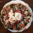 Overhead view of pizza topped with fried eggs and breakfast meats