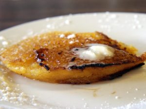 A single jonnycake, topped with melting butter, exhibits a fine, crisp edge.