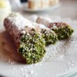 Crisp pastry tubes are filled with sweet cheese and their ends dipped in green pistachio crumbs