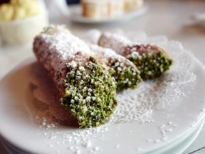 Crisp pastry tubes are filled with sweet cheese and their ends dipped in green pistachio crumbs