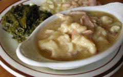 Oblong bowl of chicken and dumplings and gravy is backed by turnip greens, creamed corn, and beans.