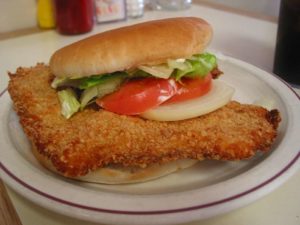 Crisp-fried tenderloin, topped with tomato, onion, and lettuce, extends far beyond the burger bun that holds it