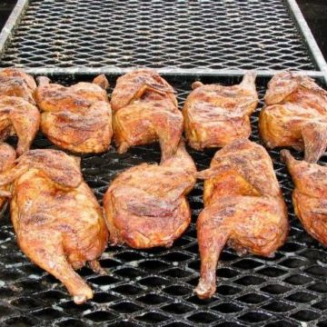 Half chickens, basted with marinade, cook on a charcoal grill